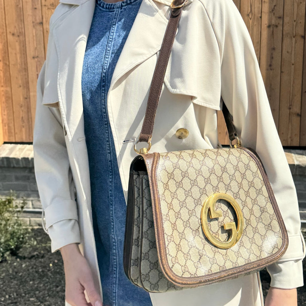 A spring model wearing a designer trench coat with a preowned Gucci handbag over their shoulder 